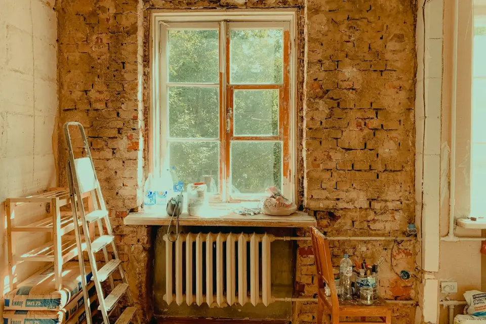 Een kamer in verbouwing met de kale bakstenen buitenmuur, een raam en een radiator