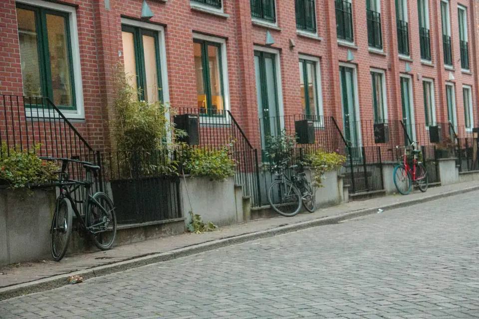 Een straat met bakstenen rijtjeshuizen, hoge ramen en een fiets tegen een hek, op een stoep van klinkers
