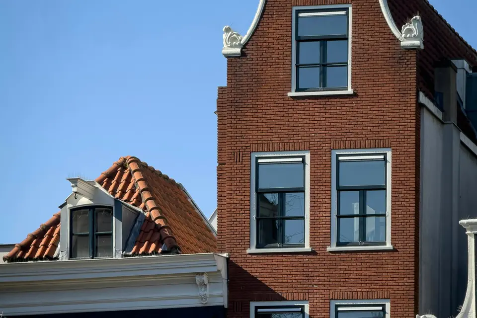 Een bakstenen halsgevel naast een dak met oranje pannen, tegen een blauwe lucht
